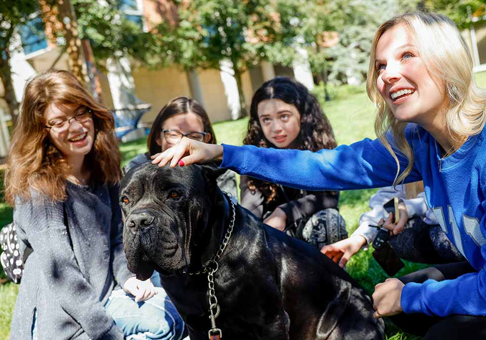 A group of students smile as one pets a large black dog.