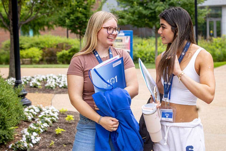 A female student smiles and sits in a circle with other members of her SLU 101 group. Other students, including her SLU 101 leader, can be seen in the foreground.