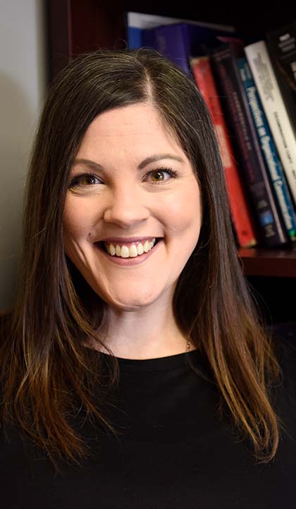 A portrait of Jennifer Ohs, Ph.D. in front of a bookcase