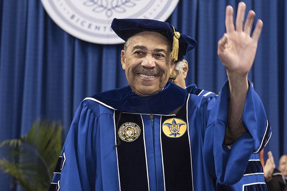 William Clay waves while wearing academic regalia.