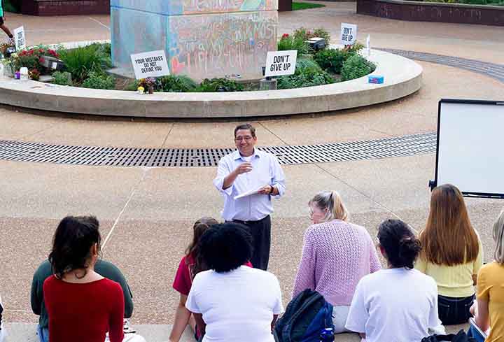 A professor stands in front of an outdoor class with at SLU's clocktower