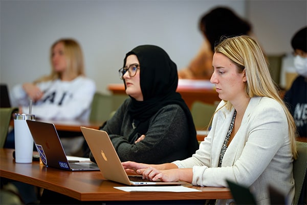 Two female students sit at a table in a classroom at Scott Hall during a class.