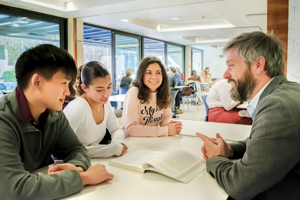 A professor is talking to three students in an area of the cafeteria.