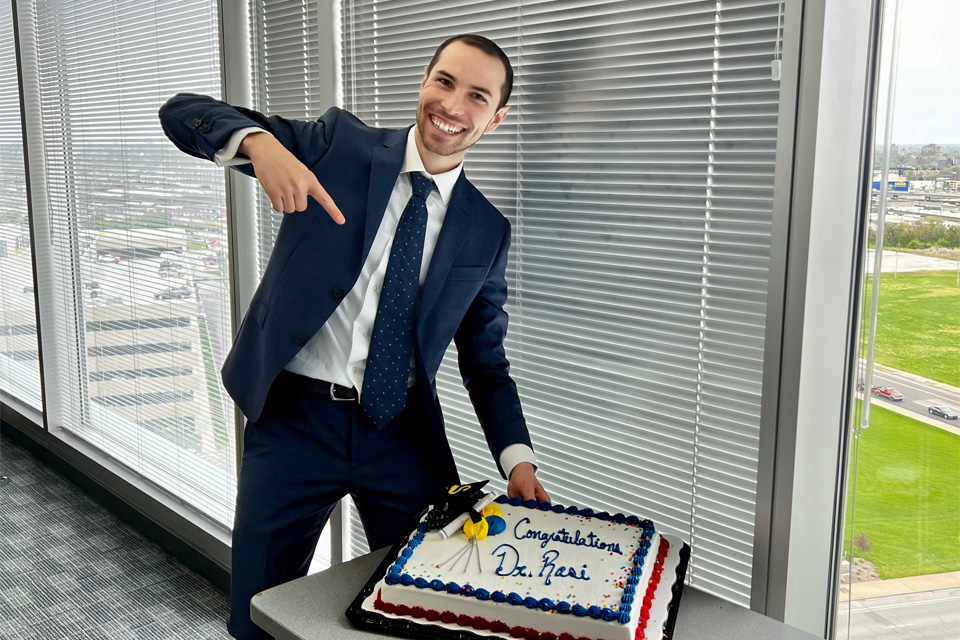 Valerio Rossi celebrating, holding a sheet cake with the words "Congratulations Valerio" iced on the top of the cake