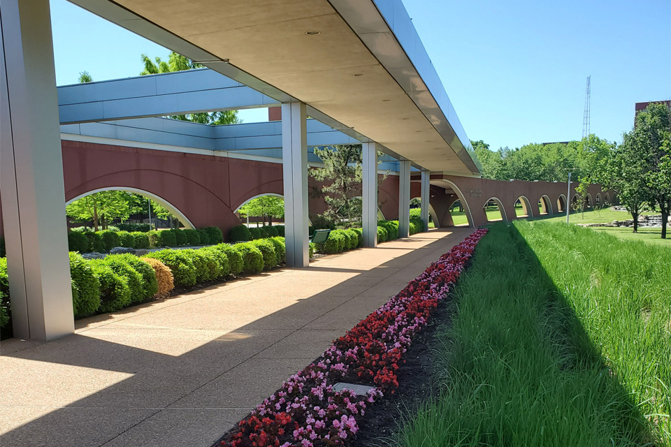 A covered walkway lined by flowers and greenery.