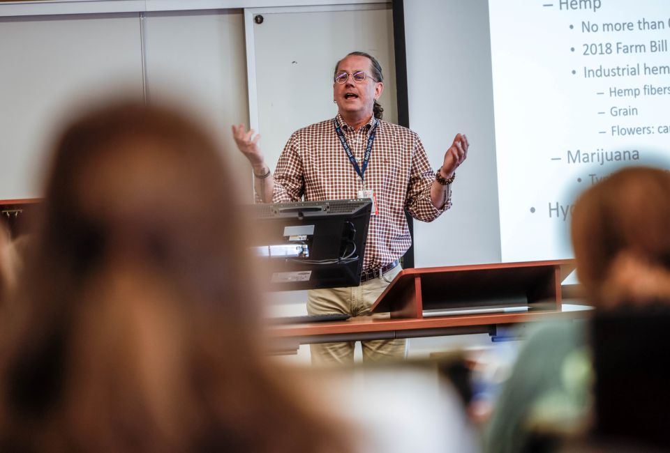 a man speaks in front of a crowd in a classroom
