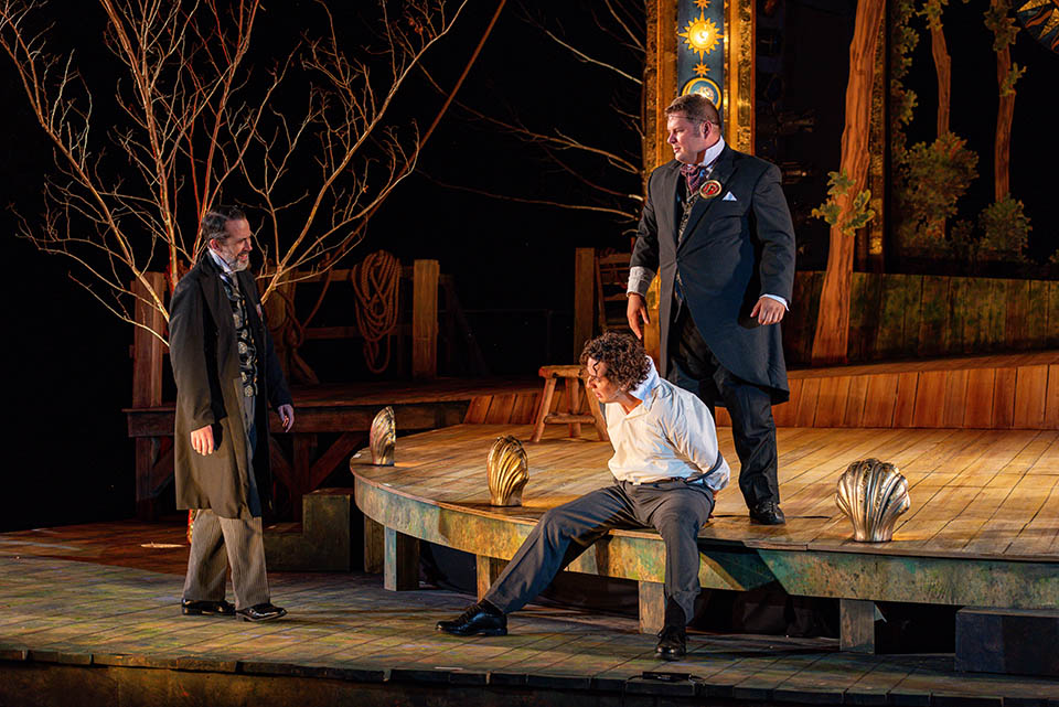 Three actors on a stage in a dimly lit theater.