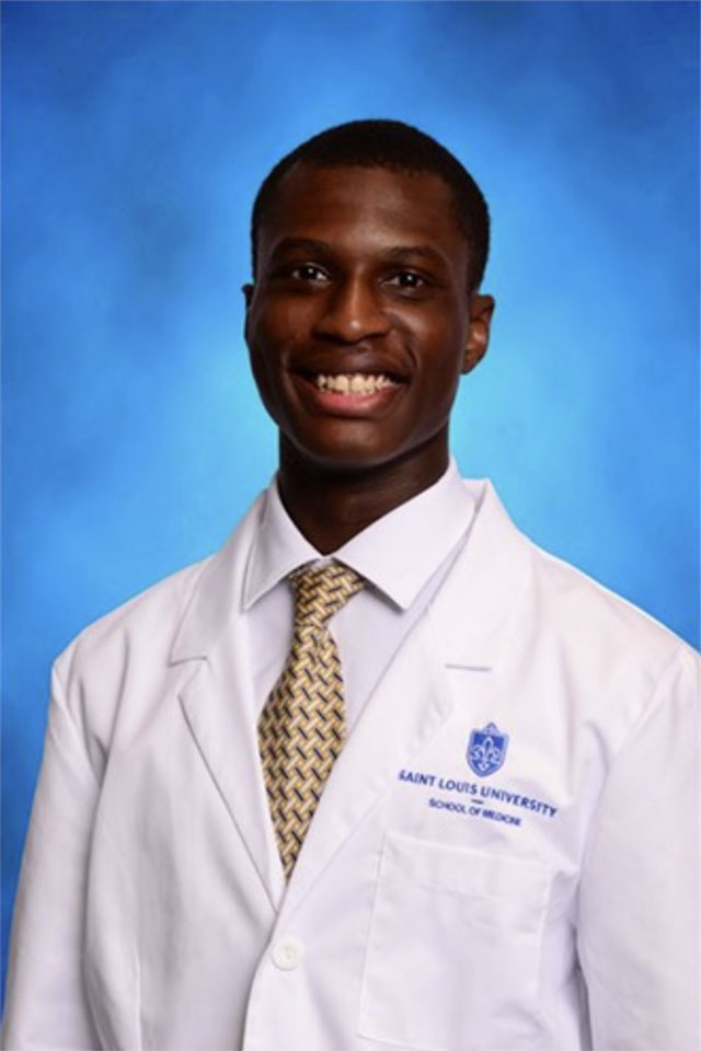 Abdul-Haq Alli poses for a photo in a white coat against a blue background.