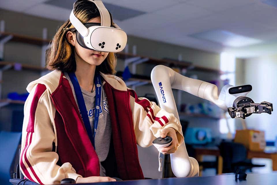 SLU mechanical engineering student use virtual-reality goggles and a controller to operate a robotic arm.