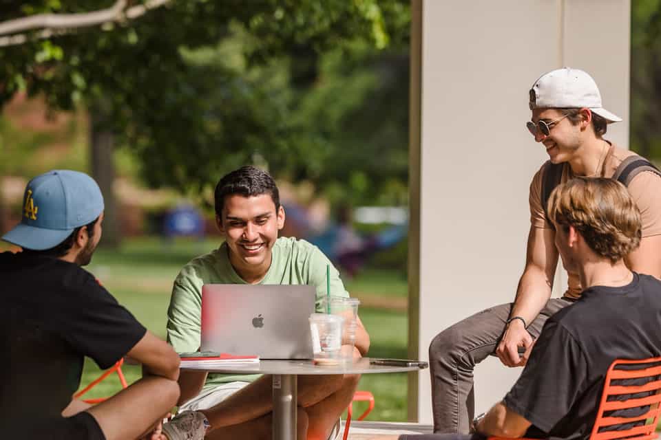 A group of four students outside with laptop at table outside SLU Pius library